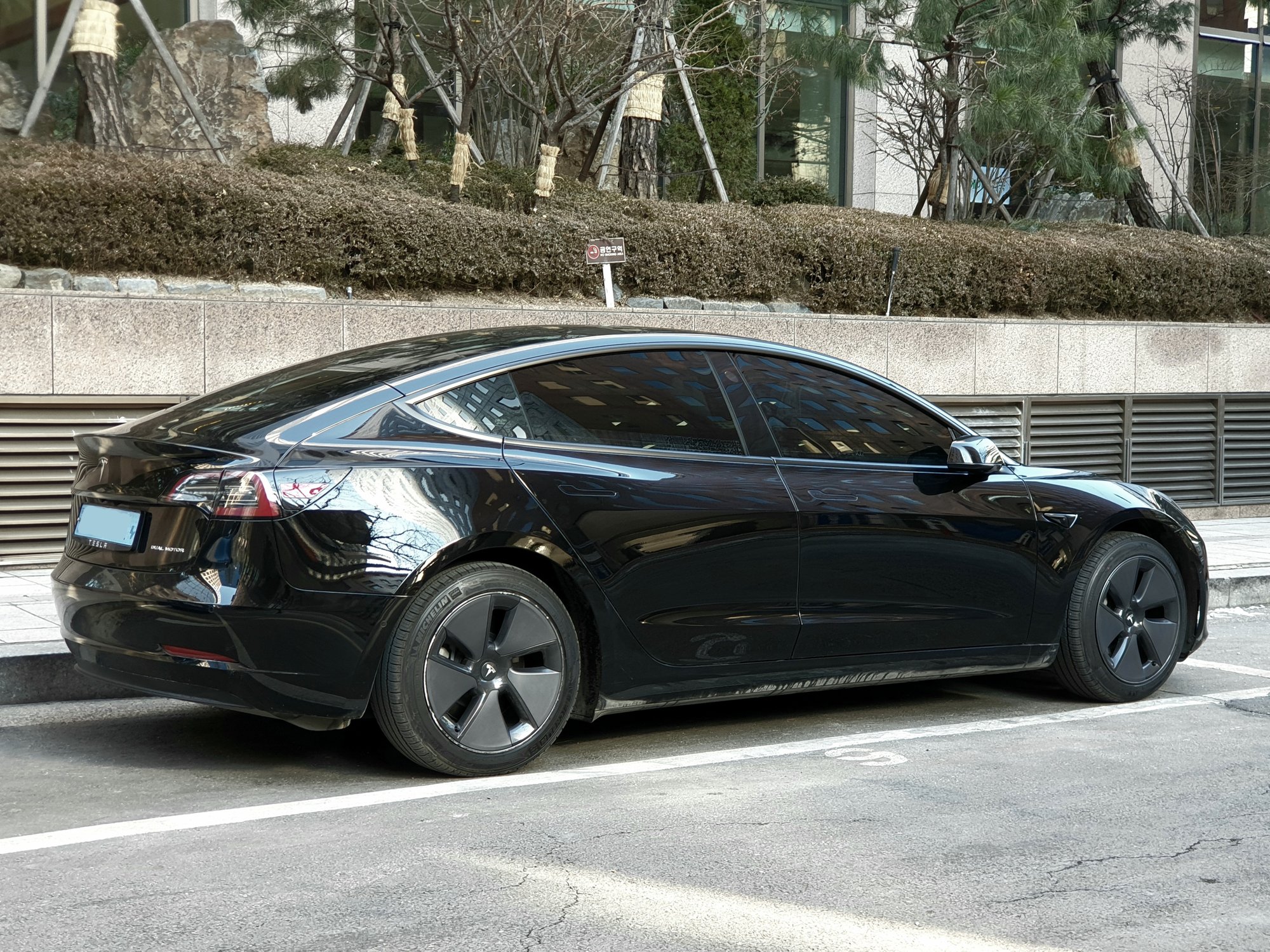 Glossy black Tesla Model 3, three-quarter rear view.