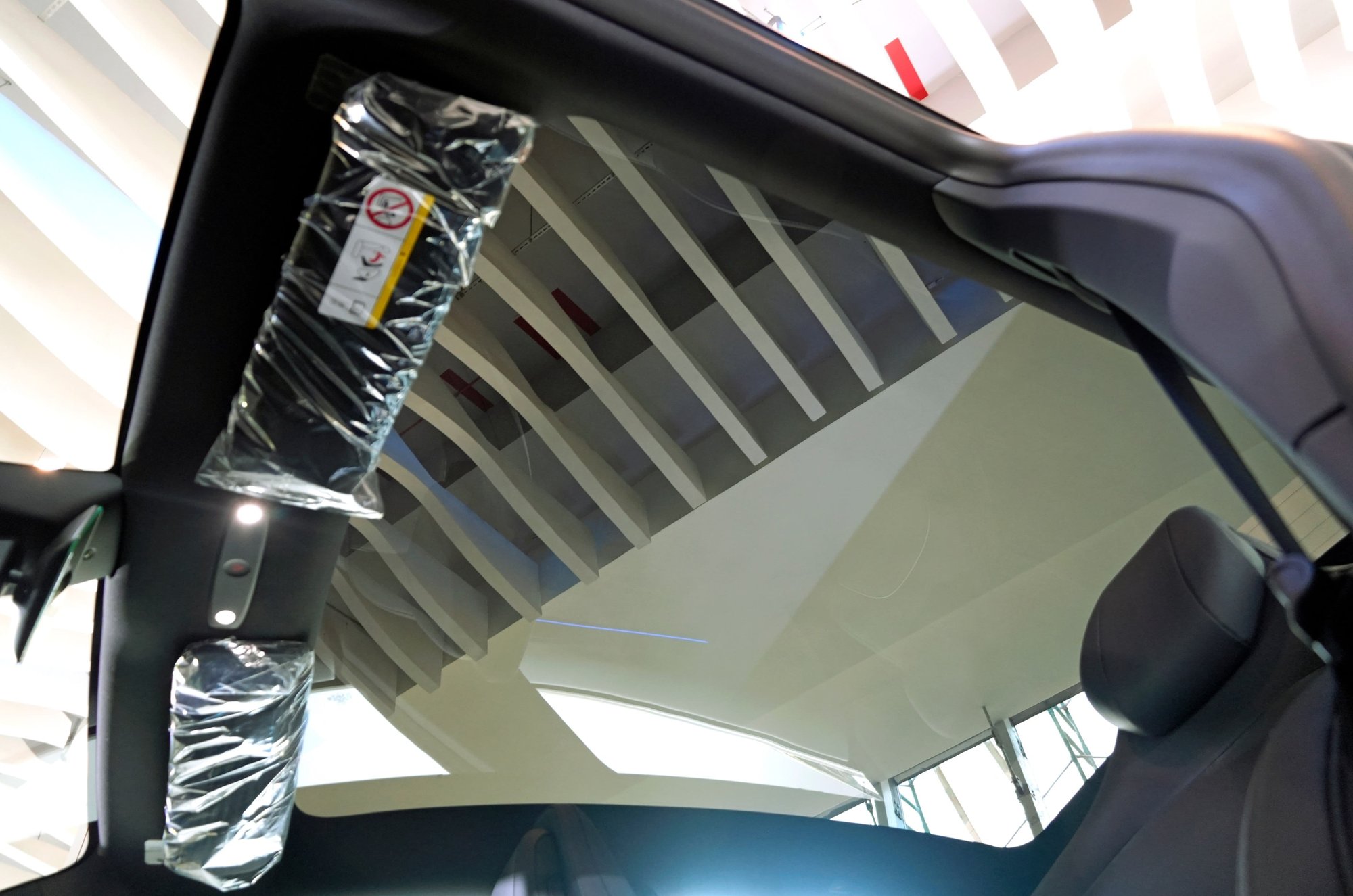 Tesla Model Y L looking up through panoramic glass with factory black headliner, visors, and pillars.