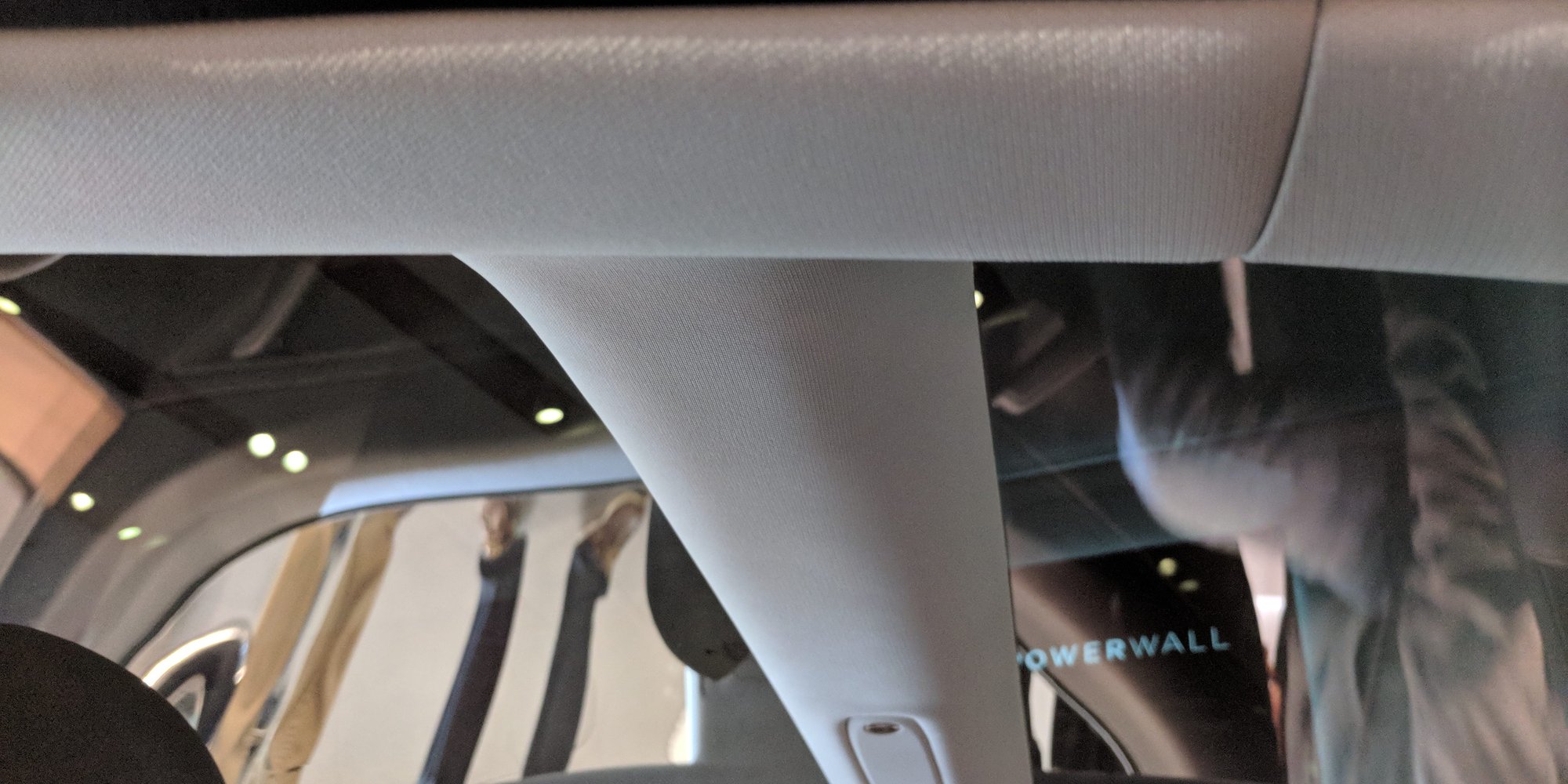 Tesla Model 3 looking up at factory light-grey headliner cloth and roof rail around the glass, through 2025.